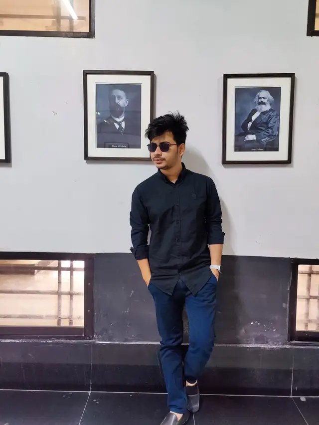Naim Bin Hasan beneath portraits of classical sociologists at the University of Dhaka.